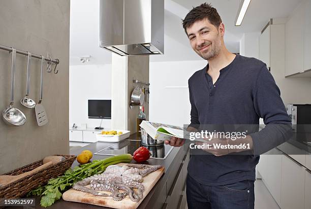 germany, cologne, mid adult man with cook book in kitchen, portrait - kochbuch stock-fotos und bilder