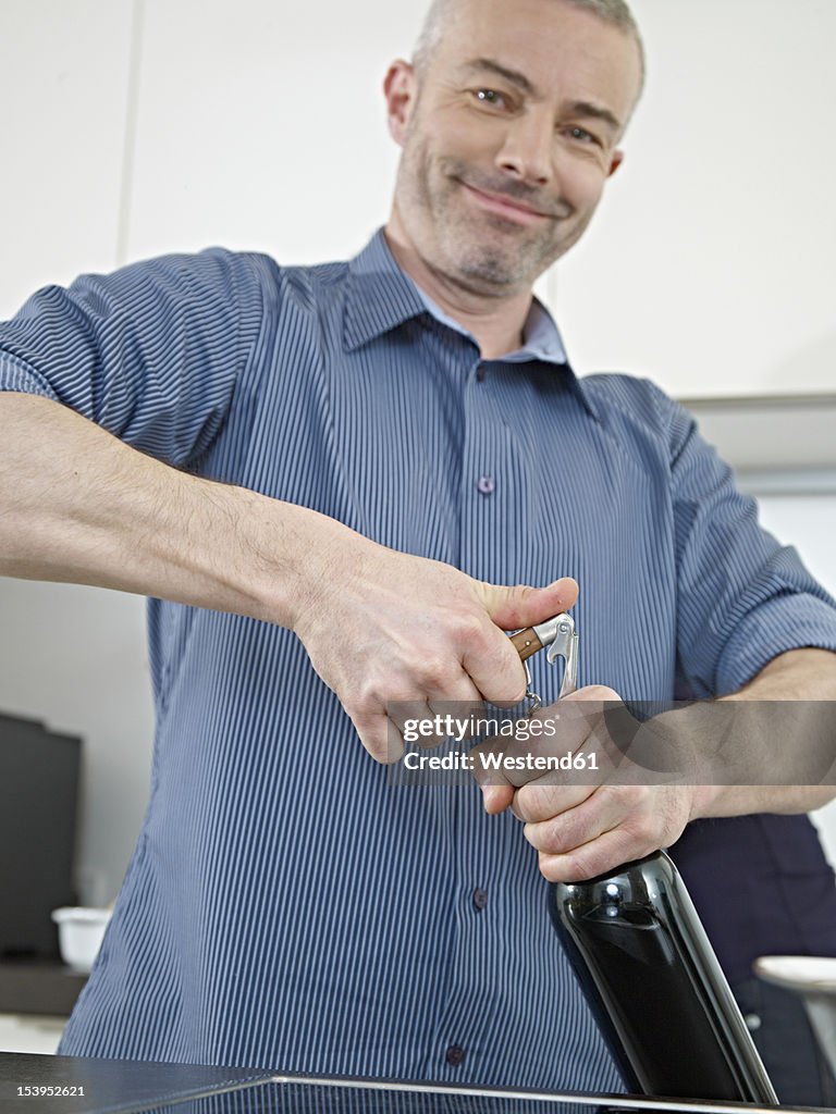 Germany, Cologne, Mature man opening wine bottle, smiling, portrait