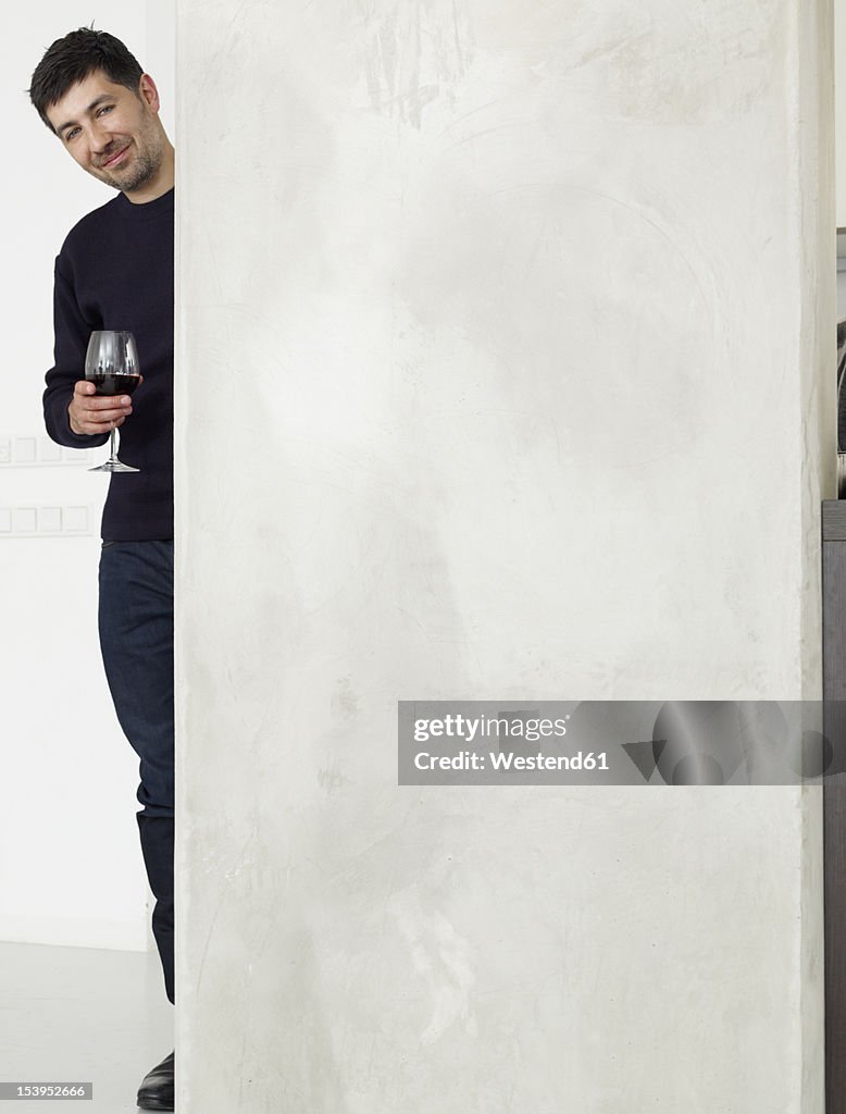 Germany, Cologne, Mid adult man drinking wine in kitchen, smiling, portrait