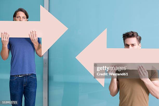 germany, north rhine westphalia, duesseldorf, young men holding arrows with different direction, portrait - north arrow stock pictures, royalty-free photos & images