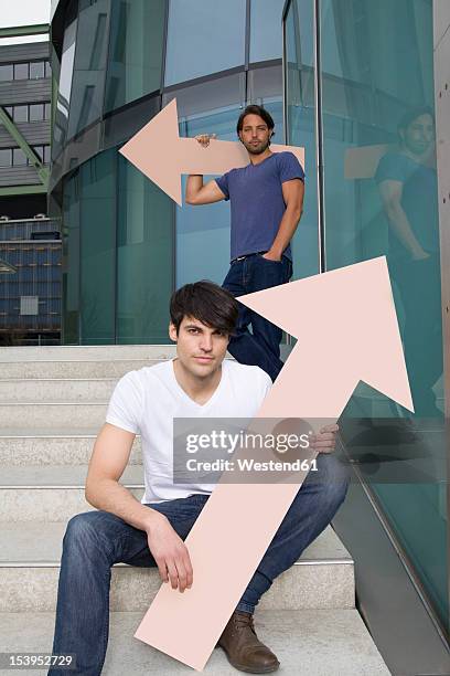 germany, north rhine westphalia, duesseldorf, young men holding arrows with different direction, portrait - north arrow stock pictures, royalty-free photos & images