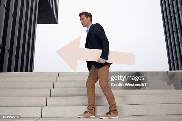 germany, north rhine westphalia, duesseldorf, young businessman walking on steps with arrow - north arrow stock pictures, royalty-free photos & images