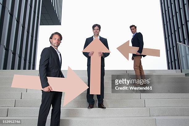 germany, north rhine westphalia, duesseldorf, young businessmen standing on steps with arrows in different directions - north arrow stock pictures, royalty-free photos & images
