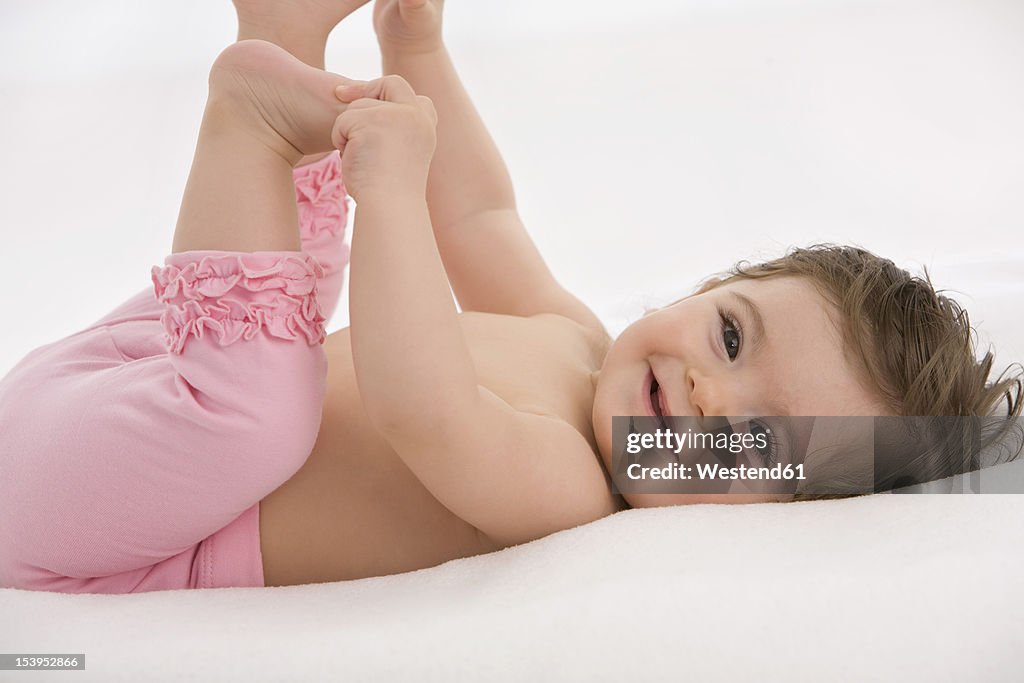 Baby girl lying on back and holding toes, smiling