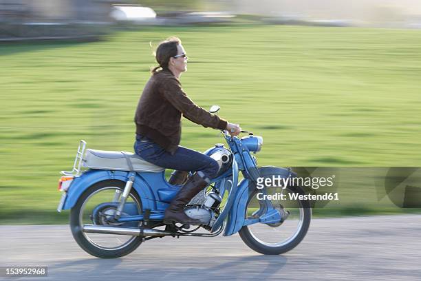 germany, bavaria, mature woman riding old moped of 1960s - moped stock-fotos und bilder