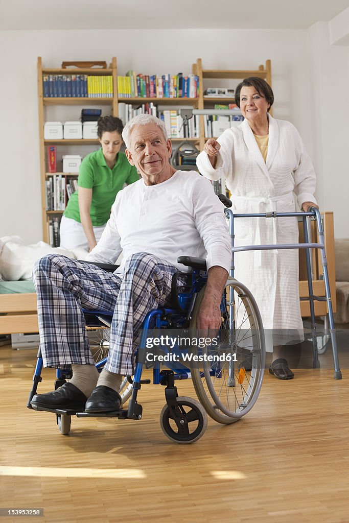 Germany, Leipzig, Senior man sitting on wheelchair, woman with walking frame