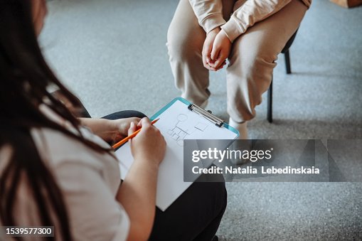 Psychologist's hands draw genogram on clipboard. Teen patient sits opposite with folded arms.Close-up. Psychologist's hands draw genogram on clipboard. Teen patient sits opposite with folded arms.Close-up.