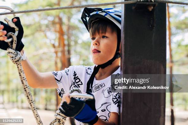 concentrated boy in a helmet enjoying activity in a climbing adventure park on a summer day. children kids activities concept - extreem weer stock pictures, royalty-free photos & images