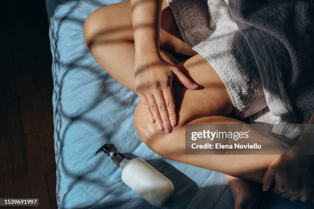 skin and body care woman hands applies  moisturizing lotion to her legs and thighs after showering or a protective product after tanning shadow overlay - thigh human leg stock pictures, royalty-free photos & images