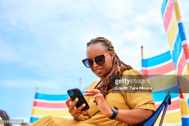 woman looking at phone by the seaside - beach shelter stockfoto's en -beelden