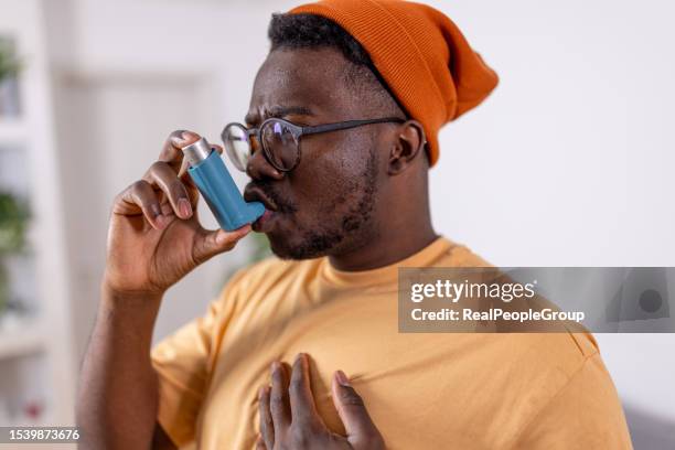 young african american man overcomes asthma challenges with inhaler at home - asthma inhaler stock pictures, royalty-free photos & images