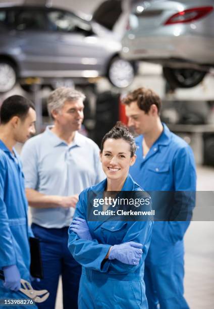 portrait of smiling female mechanic with co-workers in auto repair shop - mécanicien automobile photos et images de collection