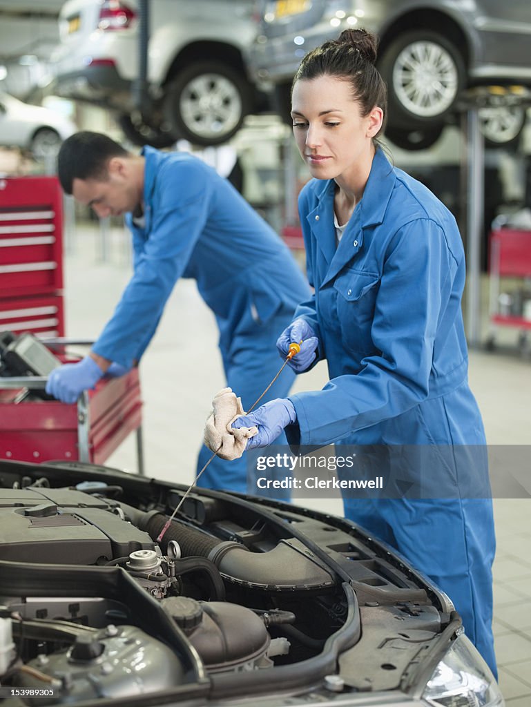 Female mechanic checking oil with dip stick in auto repair shop