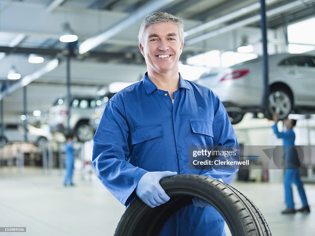 Porträt von lächelnd Mechaniker hält Reifen Sie auto repair shop