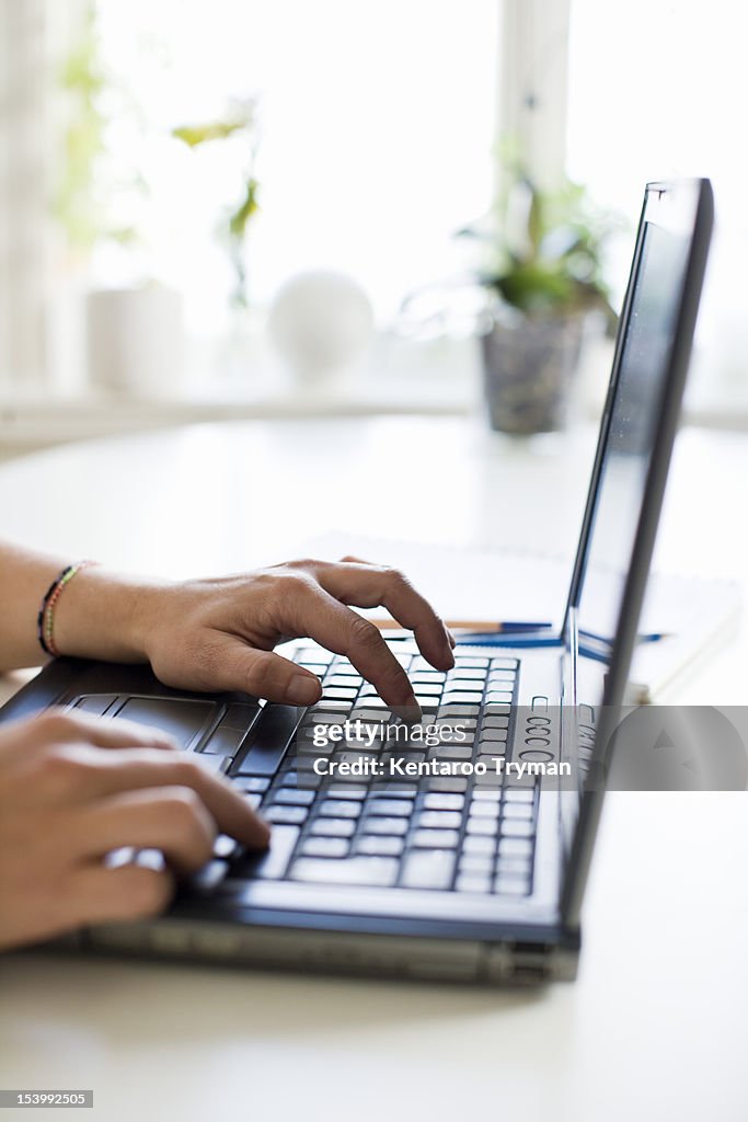 Cropped image of woman's hand typing on laptop