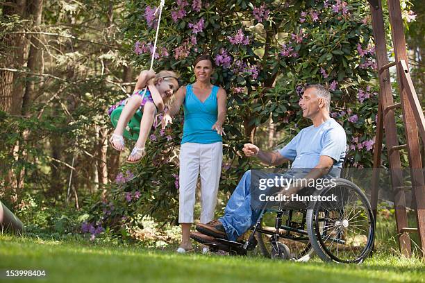 man with spinal cord injury in wheelchair watching his daughter on swing along with wife - duxbury, massachusetts stock pictures, royalty-free photos & images