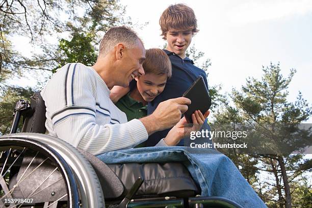 man with spinal cord injury in wheelchair with his sons reading a tablet - duxbury, massachusetts stock pictures, royalty-free photos & images