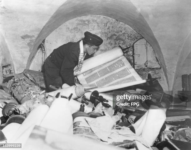 Army chaplain Samuel Blinder examines one of hundreds of Jewish Sefer Torah scrolls, stolen from all over Europe by Nazi forces, and stored in the...