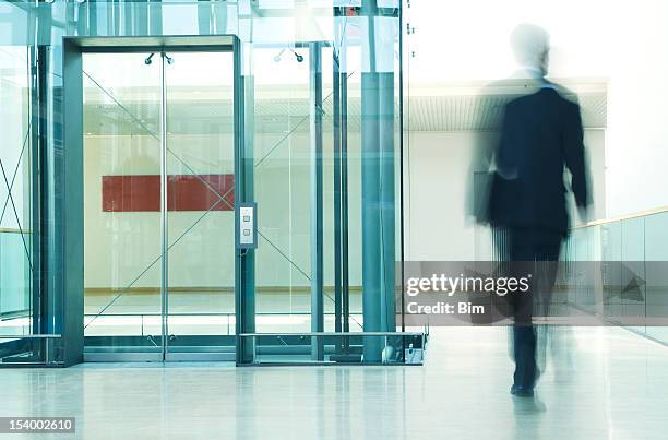 blurred businessman walking past elevator in office corridor - walking past office wall stock pictures, royalty-free photos & images