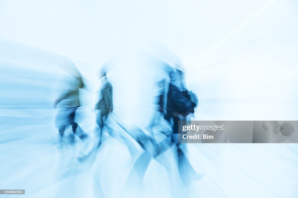 Motion Blurred Pedestrians Walking in White Hallway