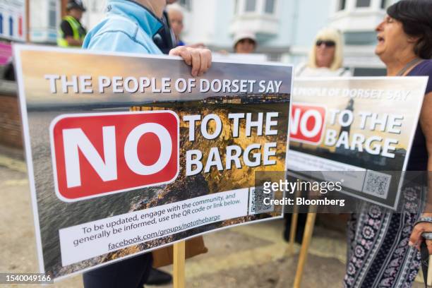 Protestors hold placards which read "No To The Barge" at Portland Port, following the arrival of the Bibby Stockholm asylum seeker accommodation...