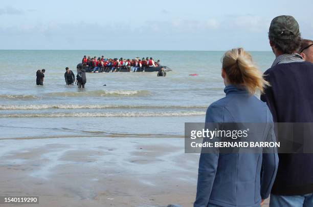 Members of the public watch as migrants sit onboard an inflatable boat before attempting to illegally cross the English Channel to reach Britain, on...