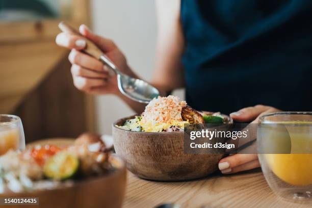 close up of young woman eating healthy and tasty poke bowl with fresh salmon and assorted vegetables on wooden table. eating out with friend in restaurant. healthy and natural eating concept - ketogenic diet stock pictures, royalty-free photos & images