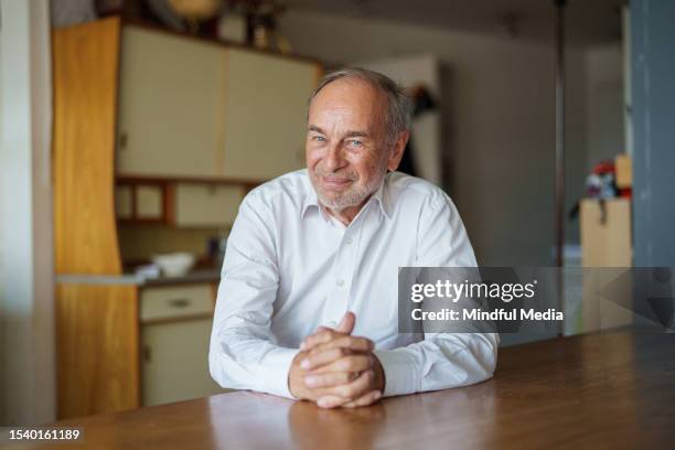 älterer mann, der in die kamera schaut, während er mit gefalteten händen sitzt - sitting at table looking at camera stock-fotos und bilder