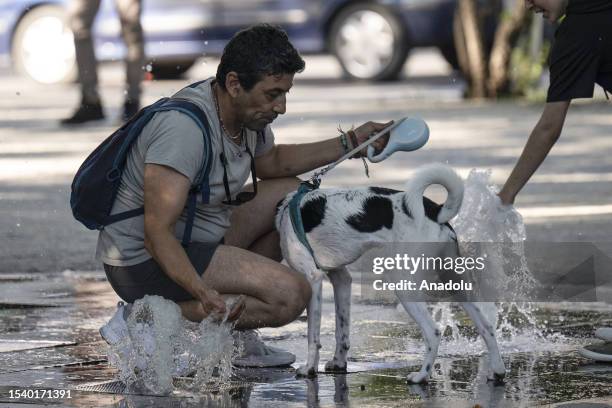 Man and a dog try to cool off near a fountain during hot weather at the Kugulu Park in Ankara, Turkiye on July 17, 2023.