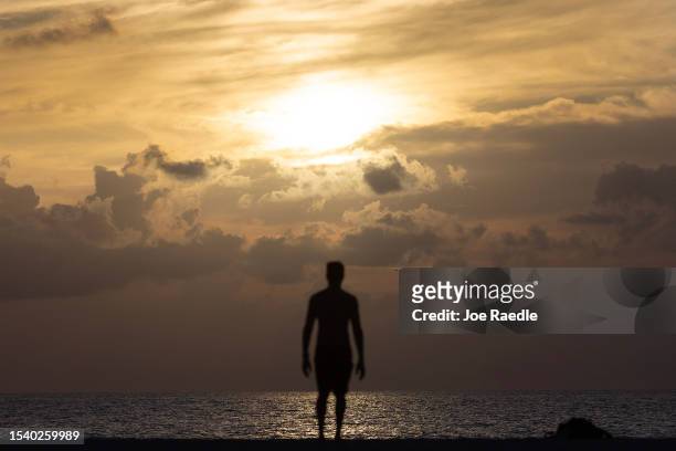 Person looks out as the sun rises over the Atlantic Ocean on July 13, 2023 in Miami Beach, Florida. With triple-digit heat indices over South...