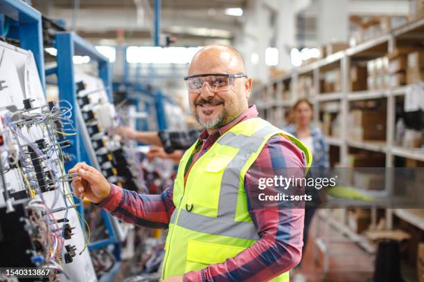 travail joyeux: un ouvrier manuel mature souriant à l’usine de fabrication - ouvrier photos et images de collection
