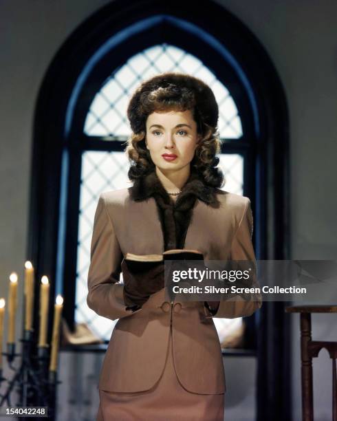 American actress Ann Blyth standing in front of a church window and holding a prayer book, in a promotional still, circa 1950.