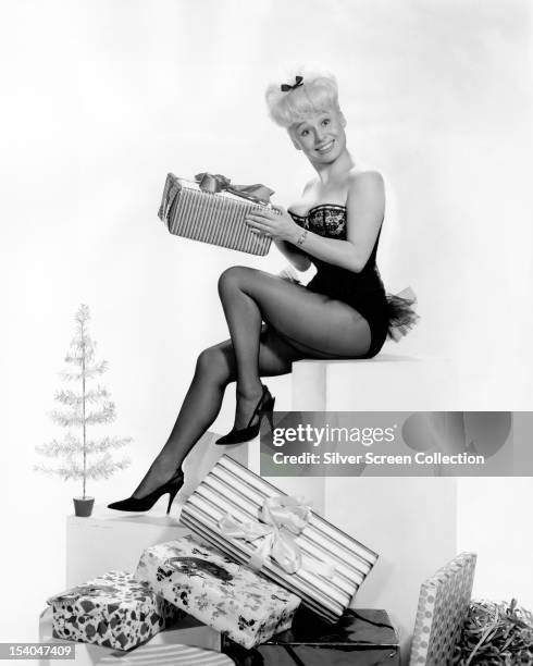 English actress Barbara Windsor wearing a basque and tights and opening Christmas presents, circa 1960.