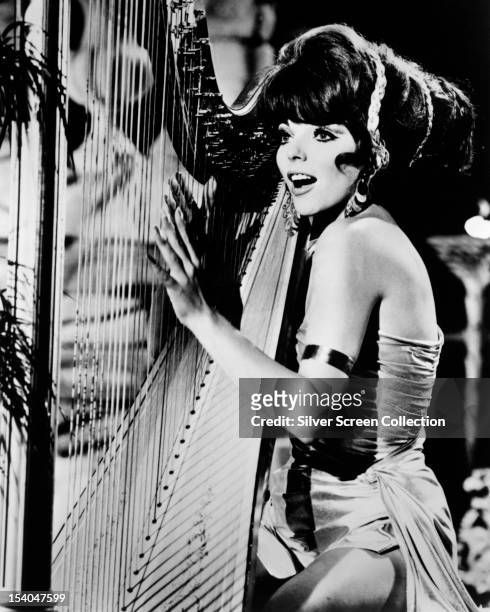 English actress Joan Collins playing a harp, as Lorelei Circe, aka Siren, in the American TV series 'Batman', 1967.