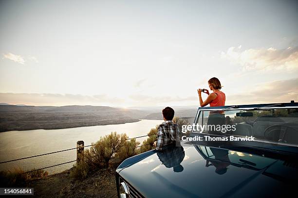 couple watching desert sunset woman taking photo - autofahrt stock-fotos und bilder