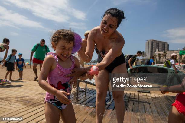 Mother cools her daughter in the public showers of the Barceloneta beach to withstand the heat on July 13, 2023 in Barcelona, Spain. An area of high...