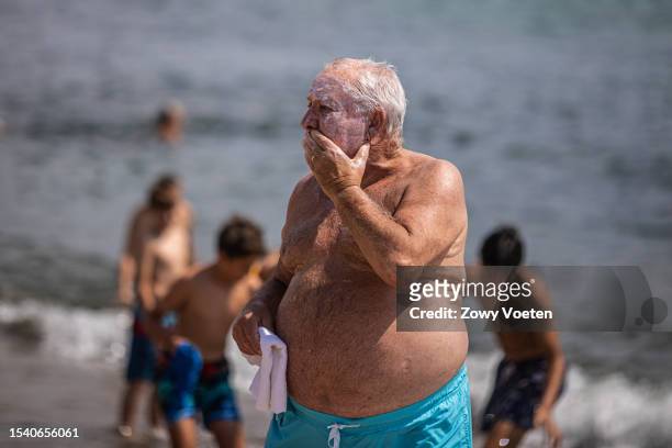 An old man fills his face with sunscreen to avoid getting sunburned on the beach of Barceloneta on July 13, 2023 in Barcelona, Spain. An area of high...