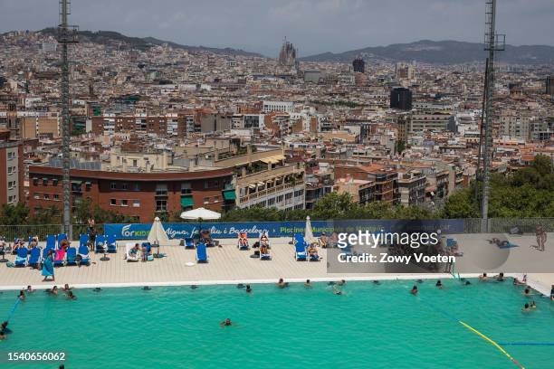 Tourists and residents enjoy the Municipal Pools of Montjuic where you can see the city of Barcelona in the background with the Basilica of the...