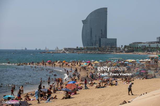 Sunbathers enjoy the sun on Barceloneta beach with the W Barcelona hotel in the background on July 13, 2023 in Barcelona, Spain. An area of high...