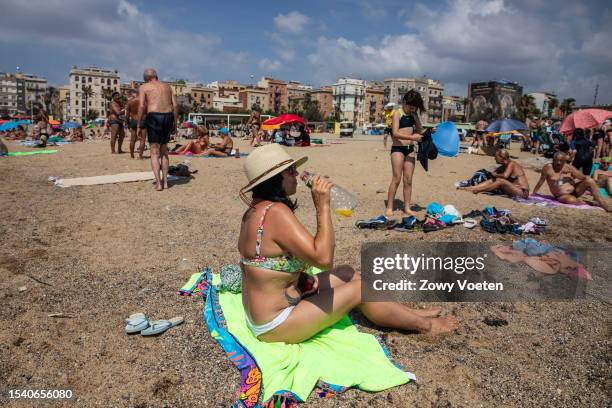 Woman drinks juice on the beach of Barceloneta to withstand the heat on July 13, 2023 in Barcelona, Spain. An area of high pressure, named Cerberus...