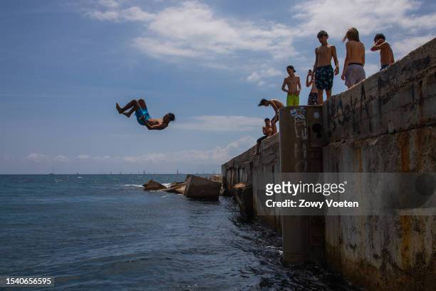 Young people enjoy jumping from the Barceloneta breakwater into the sea to withstand the midday heat on July 13, 2023 in Barcelona, Spain. An area of...