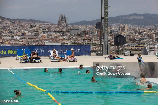 Tourists and residents enjoy the Municipal Pools of Montjuic where you can see the city of Barcelona in the background with the Basilica of the...