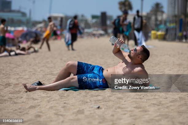Tourist cools off with a bottle of water while sunbathing on Barceloneta beach on July 13, 2023 in Barcelona, Spain. An area of high pressure, named...