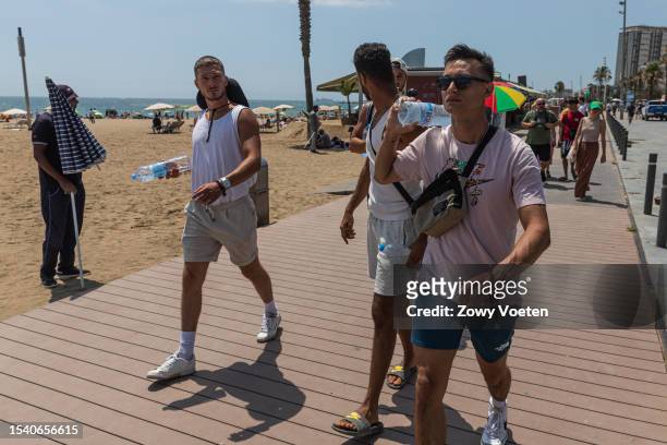 Tourists strolling along the promenade of Barceloneta beach with cold bottles of water to withstand the heat on July 13, 2023 in Barcelona, Spain. An...