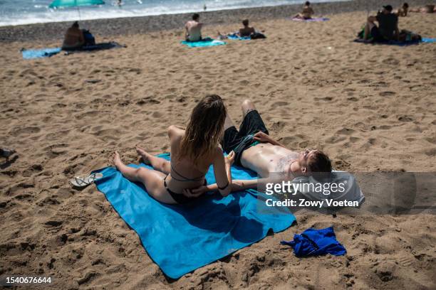 Couple enjoys the sun on the beach of Barceloneta on July 13, 2023 in Barcelona, Spain. An area of high pressure, named Cerberus after the underworld...