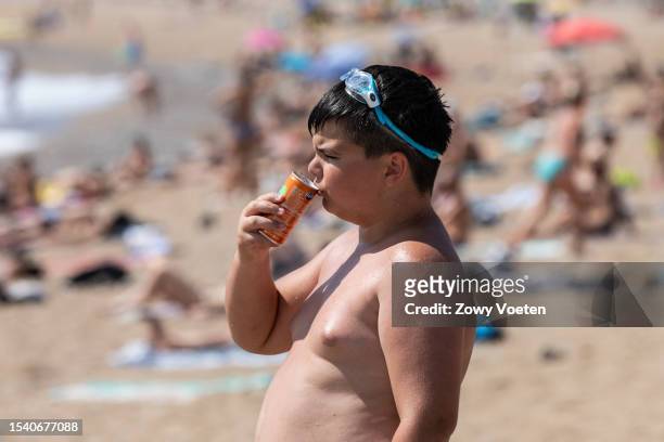 Boy drinks a soft drink on the beach of Barceloneta to withstand the heat on July 13, 2023 in Barcelona, Spain. An area of high pressure, named...