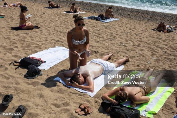 Tourist fills her partner with sunscreen to avoid getting sunburned at Barceloneta beach on July 13, 2023 in Barcelona, Spain. An area of high...