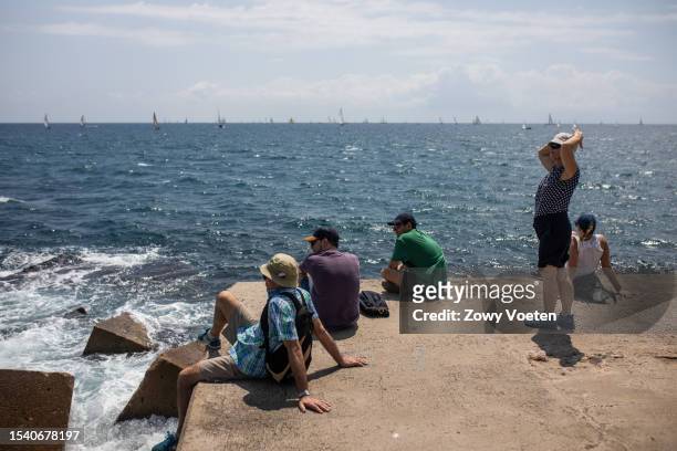 Tourists enjoy the view of the sea on a jetty at Barceloneta beach on July 13, 2023 in Barcelona, Spain. An area of high pressure, named Cerberus...