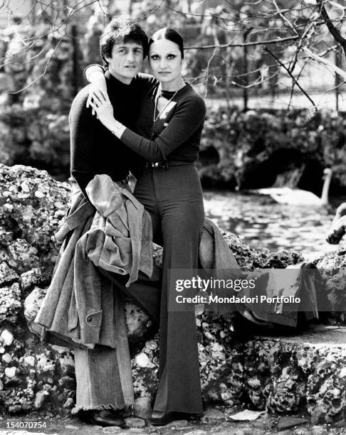 Singer Tony Renis posing for the photographer while he is hugged by his fiancee Elettra Morini at the public gardens. Milan, 1974.