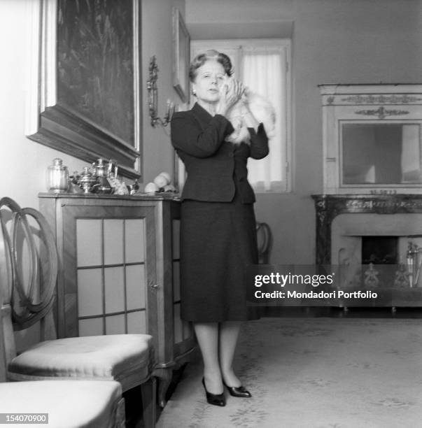 Italian writer and translator Anna Banti cuddles her white cat by the fireplace in her fashionable house in Florence embellished by many artworks....